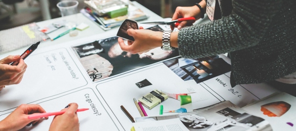 Designer cutting up printed brochure with scissors desk over desk full of brand ideas. 