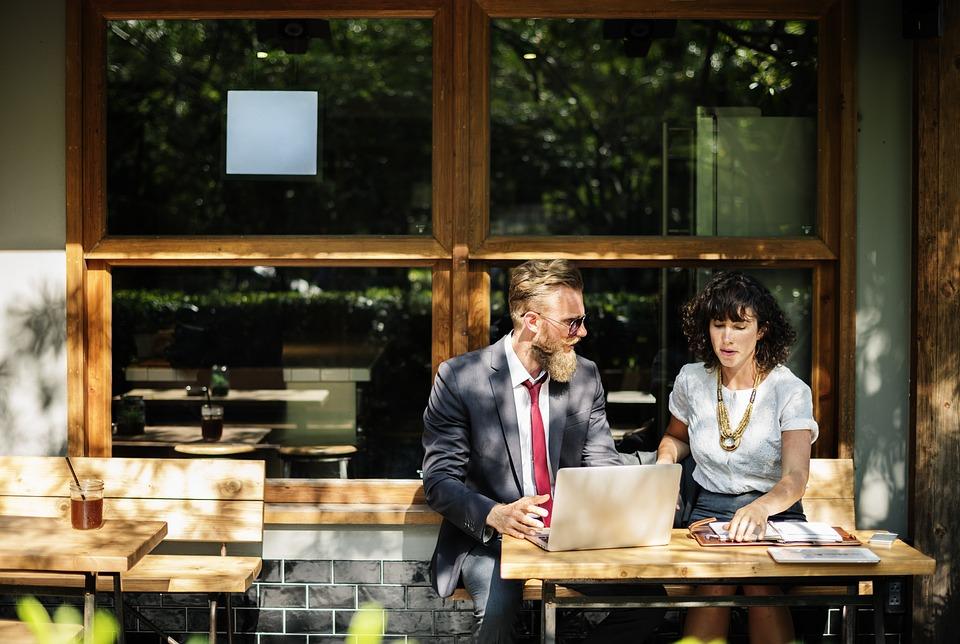 Young business man and woman looking at laptop on a patio in the sun. 