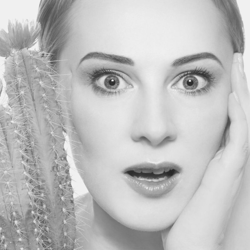 Woman's face is getting pricked by a cactus. 